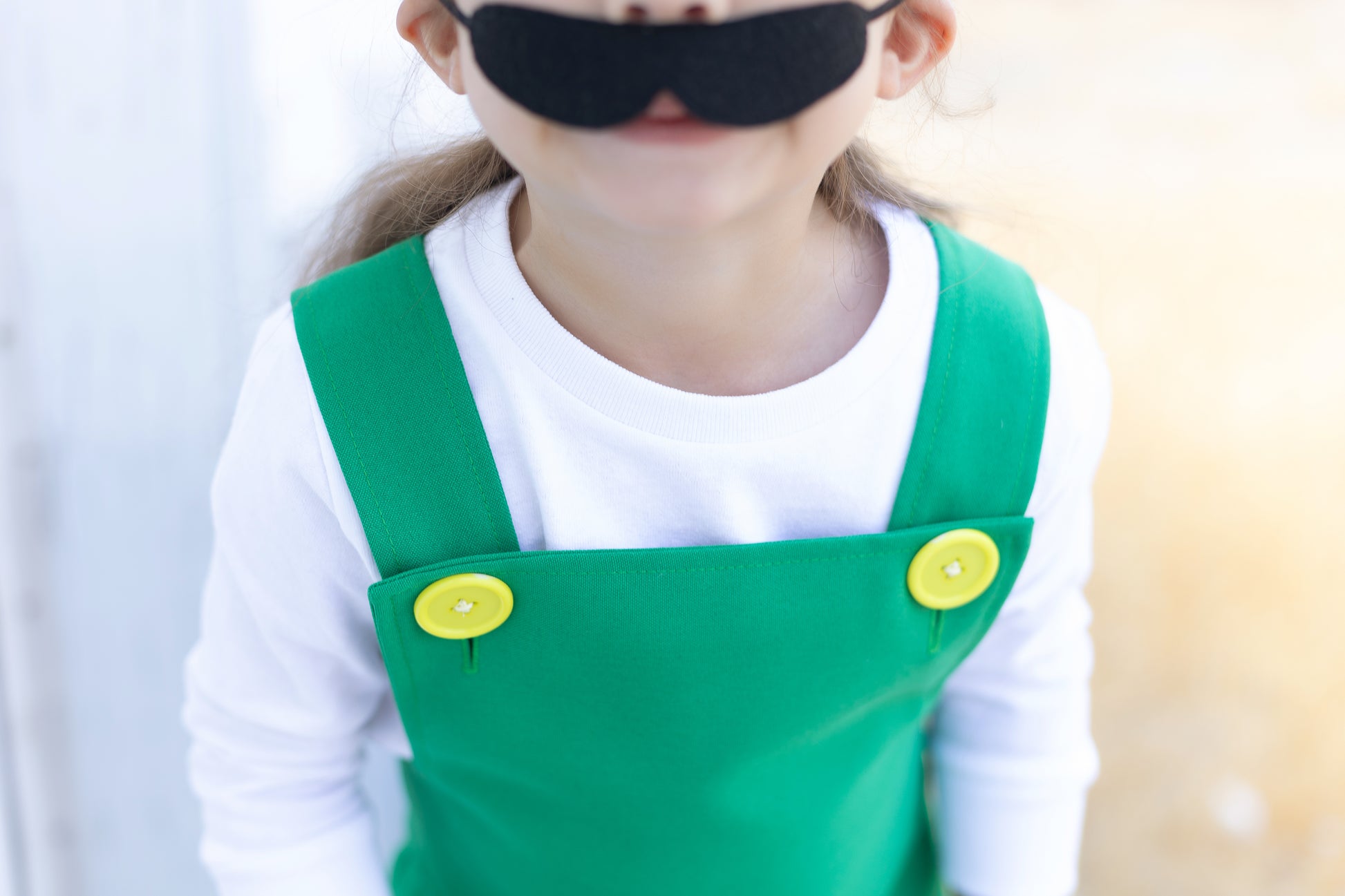 Close-up detail of handmade Fire Luigi Bros costume — green overalls with yellow buttons over a white long sleeve t-shirt, with black mustache accessory