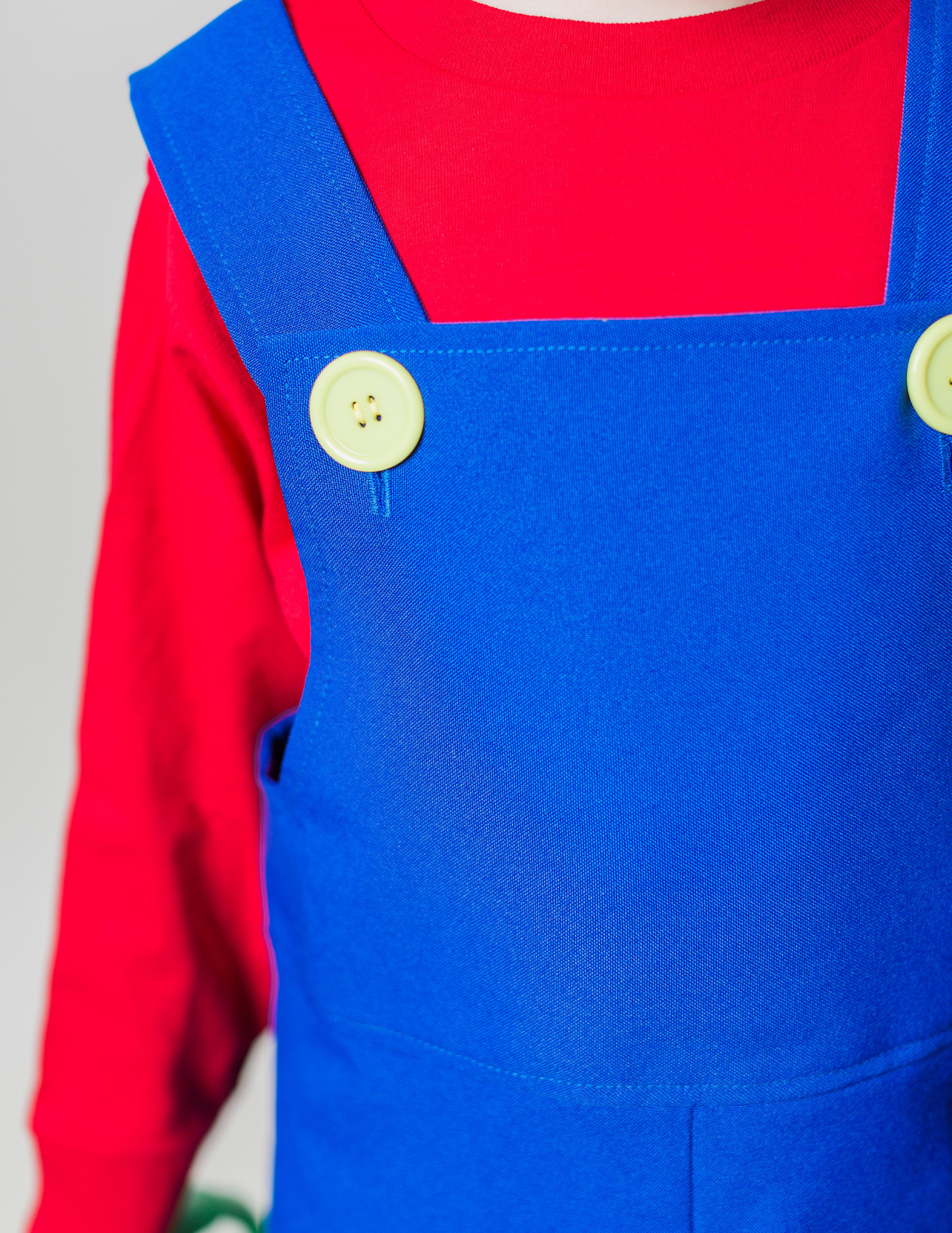 Close-up detail of handmade Mario Bros costume — blue polyester overalls with plastic yellow buttons over a red long sleeve t-shirt