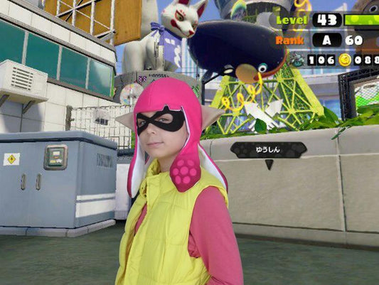 Child wearing pink Splatoon 2 Inkling cosplay hat with tentacles and pointed ears, black mask, Splatoon game background